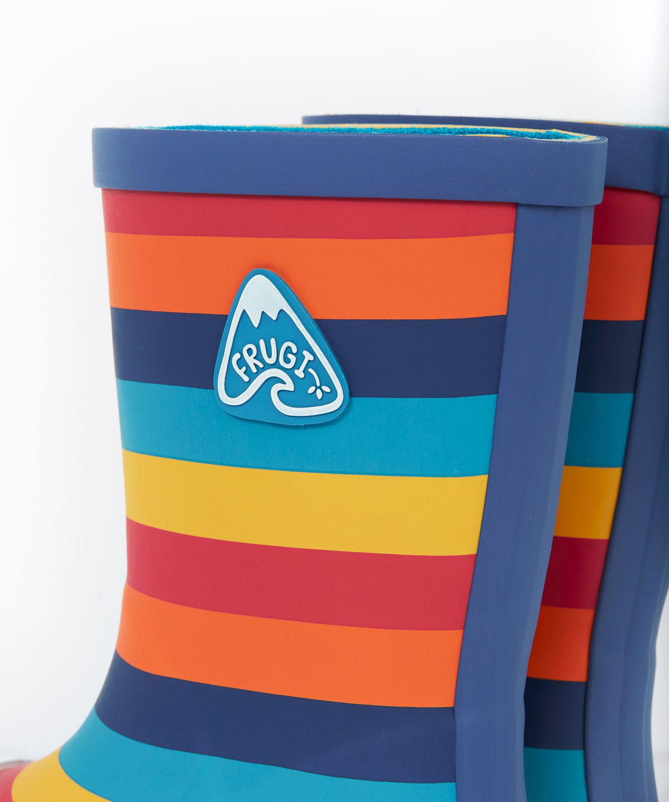 A close up of the top of the Frugi kids puddle buster wellington boots. Showing the the navy trim and rainbow inspired coloured stripes print detail on natural rubber material. Features a navy  triangular brand patch on the outside of the boot. 