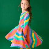 Child twirling wearing the Frugi GOTS organic cotton long sleeved sofia skater dress with a rainbow ric rac pattern.