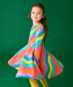 Child twirling wearing the Frugi GOTS organic cotton long sleeved sofia skater dress with a rainbow ric rac pattern.