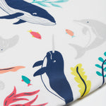 A close up of Frugi Reid Raglan T-Shirt in Soft White, featuring a Sea Life Whale print, which includes large sea animals such as the whale, and smaller fish surrounded by colourful seaweed and coral.
