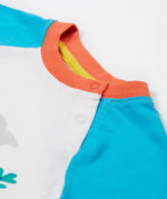 A close up of the Frugi Reid Raglan T-Shirt in Soft White featuring blue sleeves and a orange collar with popper fastenings.