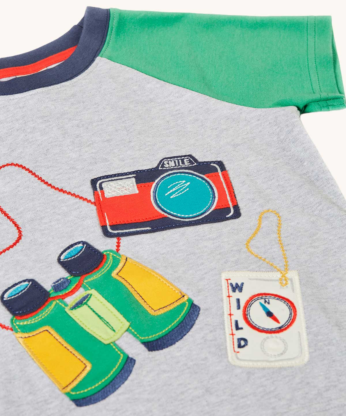 Close up of front of the Frugi raglan t-shirt featuring an adventure themed applique design on the front with a pair of green binoculars, camera and a wild card compass. 