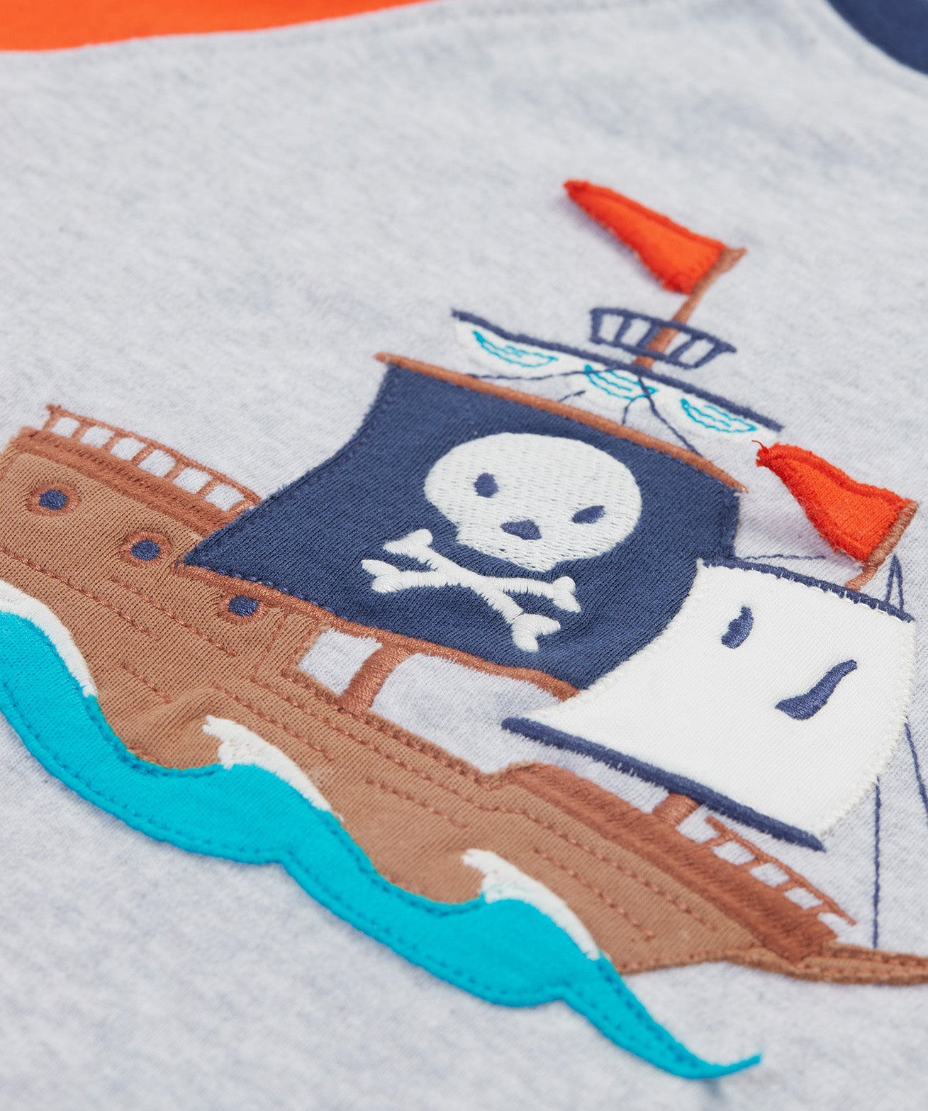 A close up of Frugi Renny Raglan T-Shirt in Grey Marl, featuring an embroidered pirate ship design in the centre.