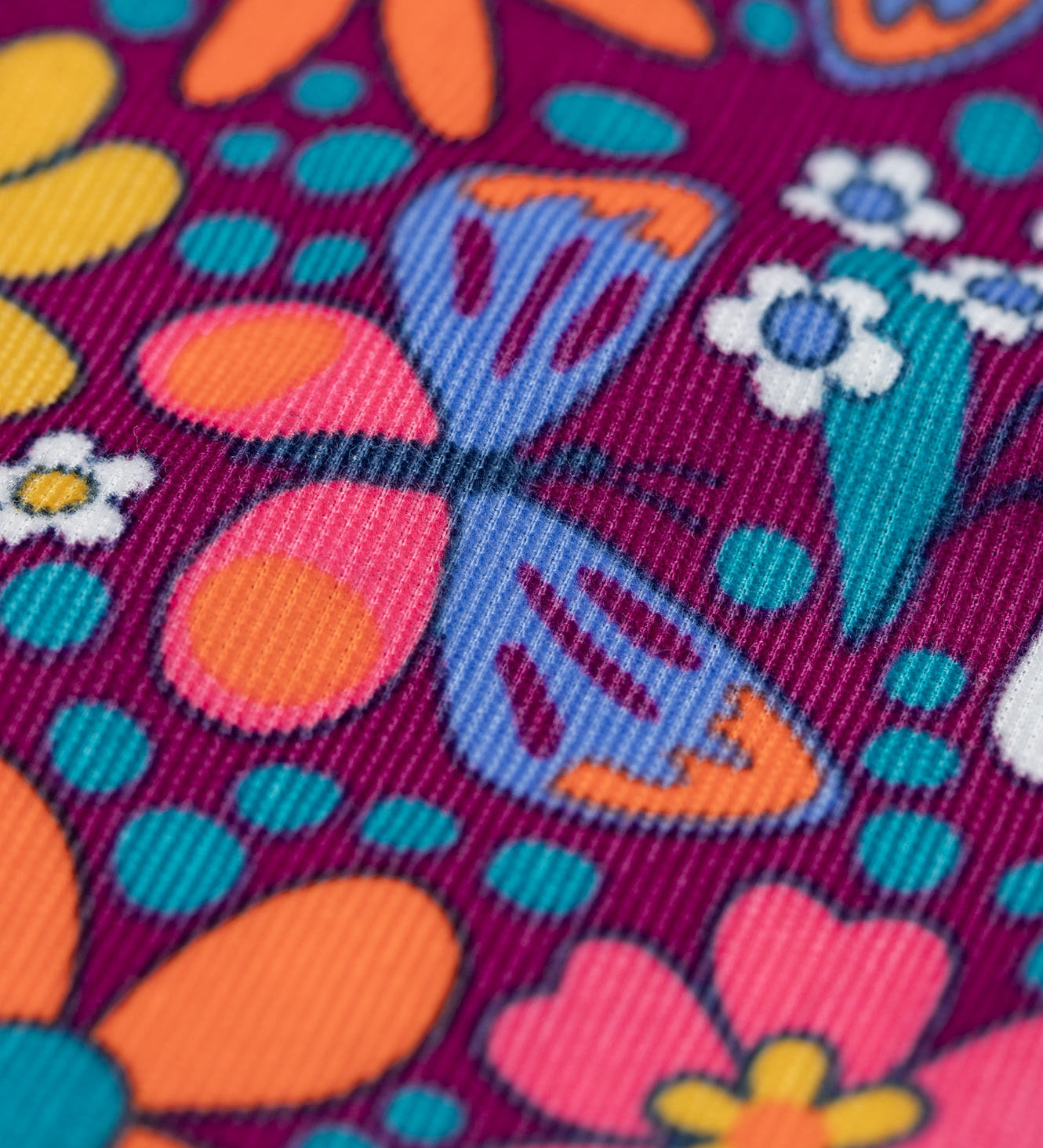 A close up of the print details on teh material of the Frugi Elspeth Retro Floral Organic Cotton Corduroy Toddler Dungarees. A purple coloured corduroy with retro flower detailing all over.  These cord dungarees are a part of a wide range of organic cotton clothing for children available here at Babipur. 
