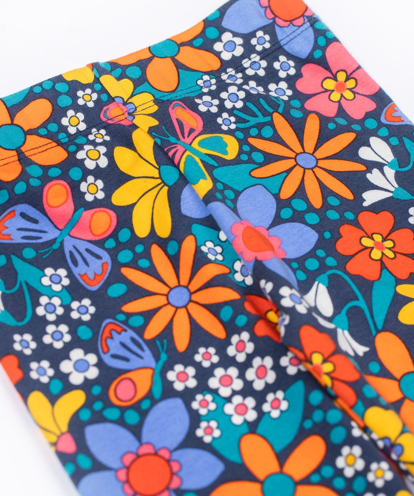 A close up of the waistband on the top of the A close up of the print on the Frugi Retro Floral Leona Organic Cotton Kids' Leggings. A navy coloured legging with a bright multicoloured retro style flower print all over. These leggings are part of a wide range of organic cotton clothing for children available here at Babipur. 