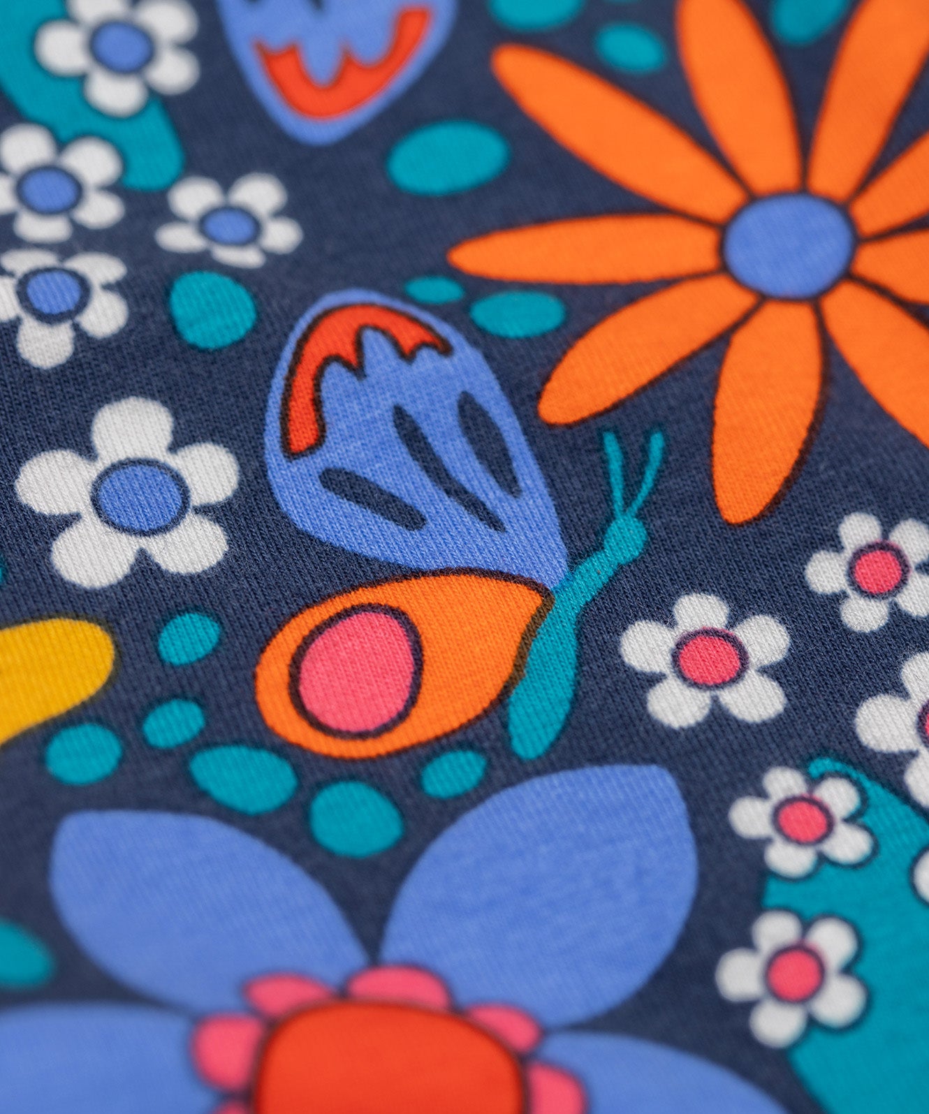 A close up of the print on the Frugi Retro Floral Leona Organic Cotton Kids' Leggings. A navy coloured legging with a bright multicoloured retro style flower print all over. These leggings are part of a wide range of organic cotton clothing for children available here at Babipur. 
