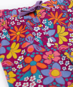 A close up of the purple waist tie on the Frugi Retro Floral print Nieva Cotton Corduroy Trousers. A purple coloured corduroy with a colourful all over floral print. These trousers are part of a wide range of organic cotton clothing for children available here at Babipur.