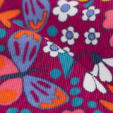 A close up view of the material of the Frugi Retro Floral print Nieva Cotton Corduroy Trousers. A purple coloured corduroy with a colourful all over floral print. These trousers are part of a wide range of organic cotton clothing for children available here at Babipur.