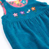 A close up of the Frugi kids reversible helen dungarees in boat blue. showing the blue corduroy and playful flower applique detail on organic cotton fabric.