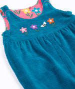 A close up of the Frugi kids reversible helen dungarees in boat blue. showing the blue corduroy and playful flower applique detail on organic cotton fabric.