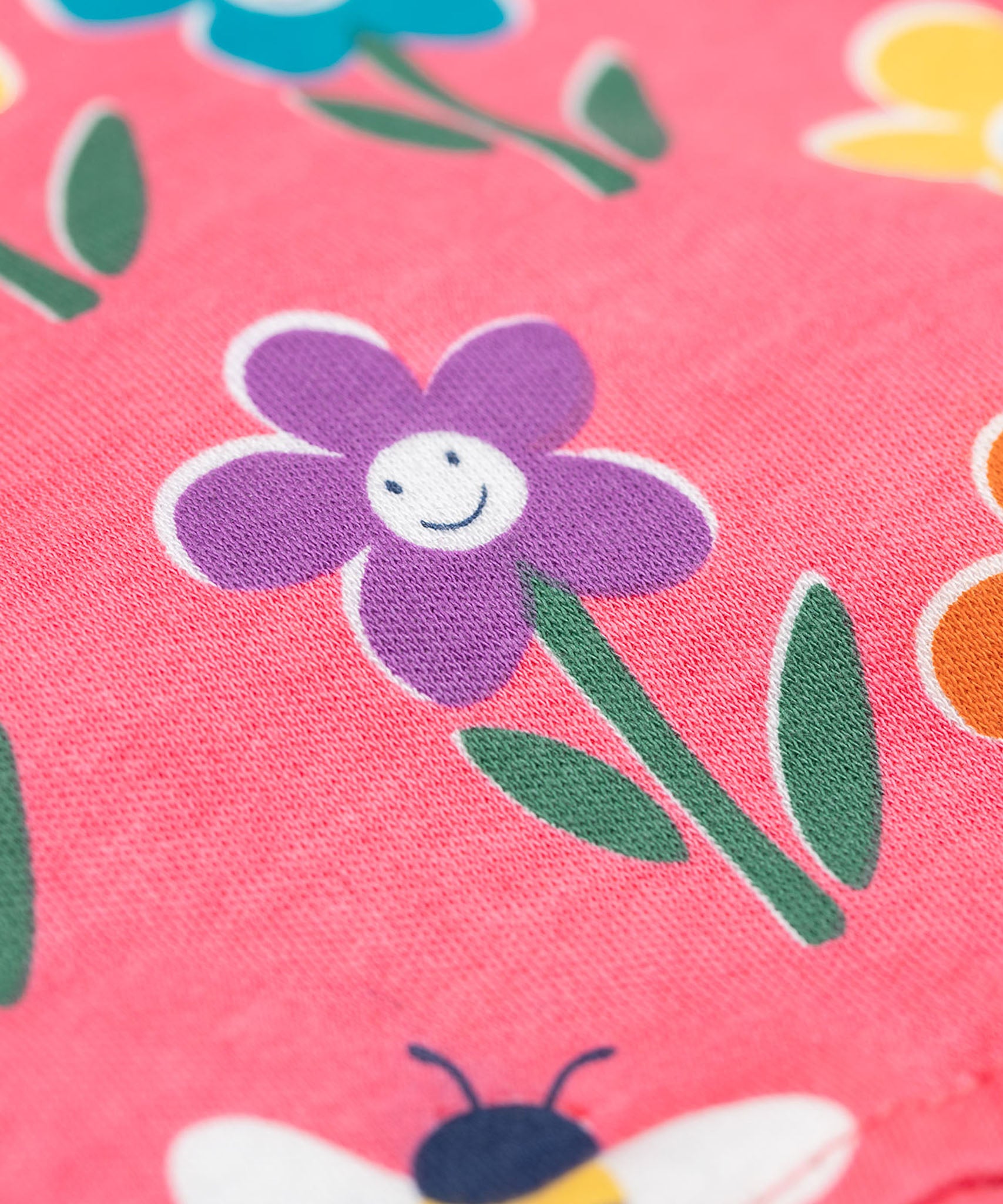A close up of the Frugi kids reversible helen dungarees in playful flowers. showing the playful flower print detail  on pink organic cotton fabric.