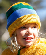 A child wearing the Frugi reversible voyager hat in penguin rainbow showing the bold yellow green and blue stripe design with a yellow soft ribbed trim.