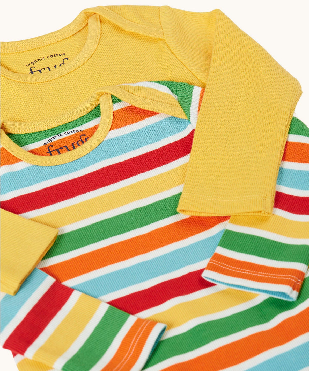 A close up of the envelope necks on the front of the Frugi ribbed material 2 pack long sleeved body vests One vest is plain yellow the other has rainbow stripes, bands of red, pastel yellow, green, orange and pastel blue in between thinner white stripes. 