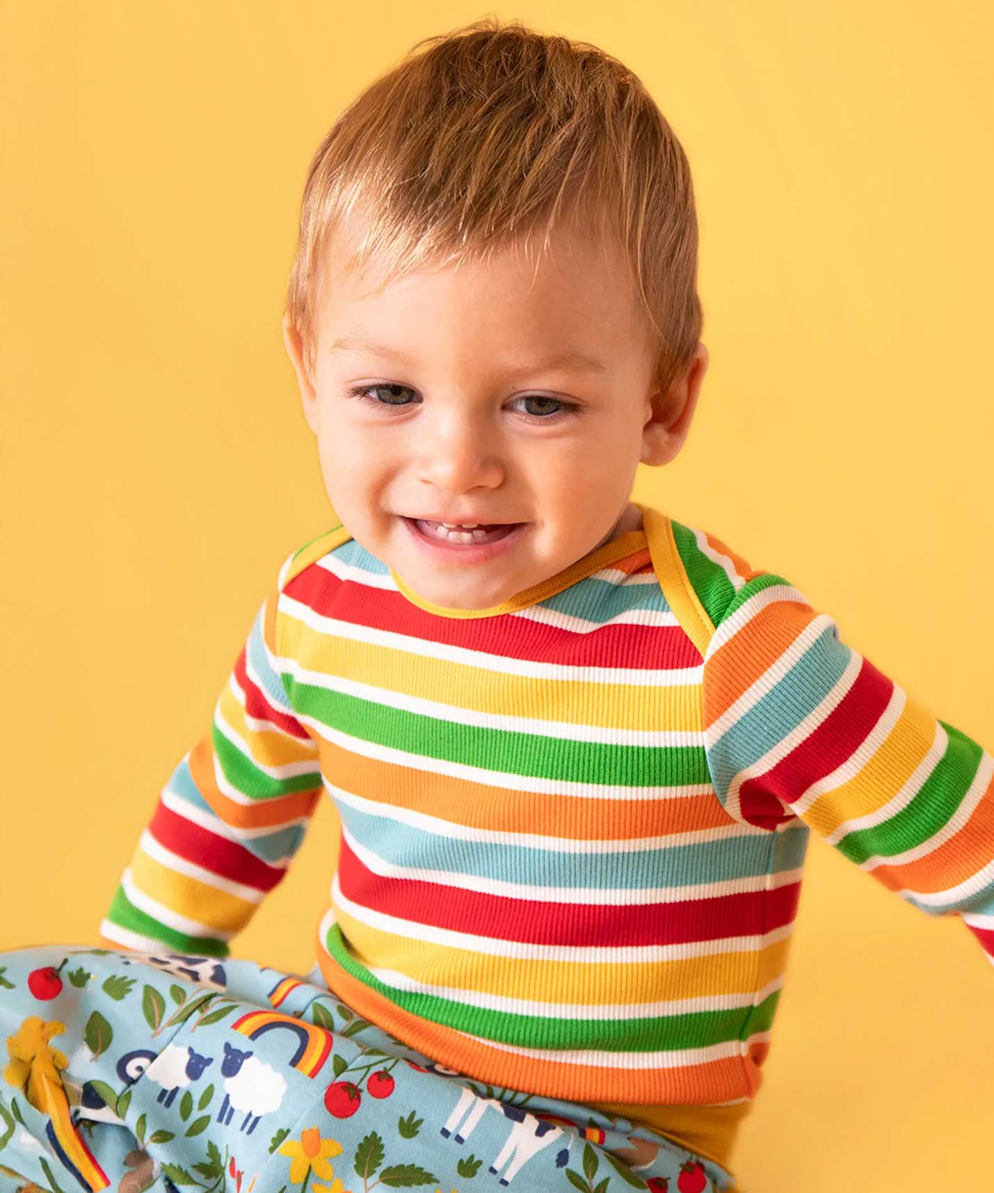 Baby wearing a Frugi rainbow striped long sleeved ribbed organic cotton vest with parsnip pants. 