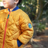 A child wearing the Frugi robin reversible quilted jacket in yellow gold with boat blue fleece.