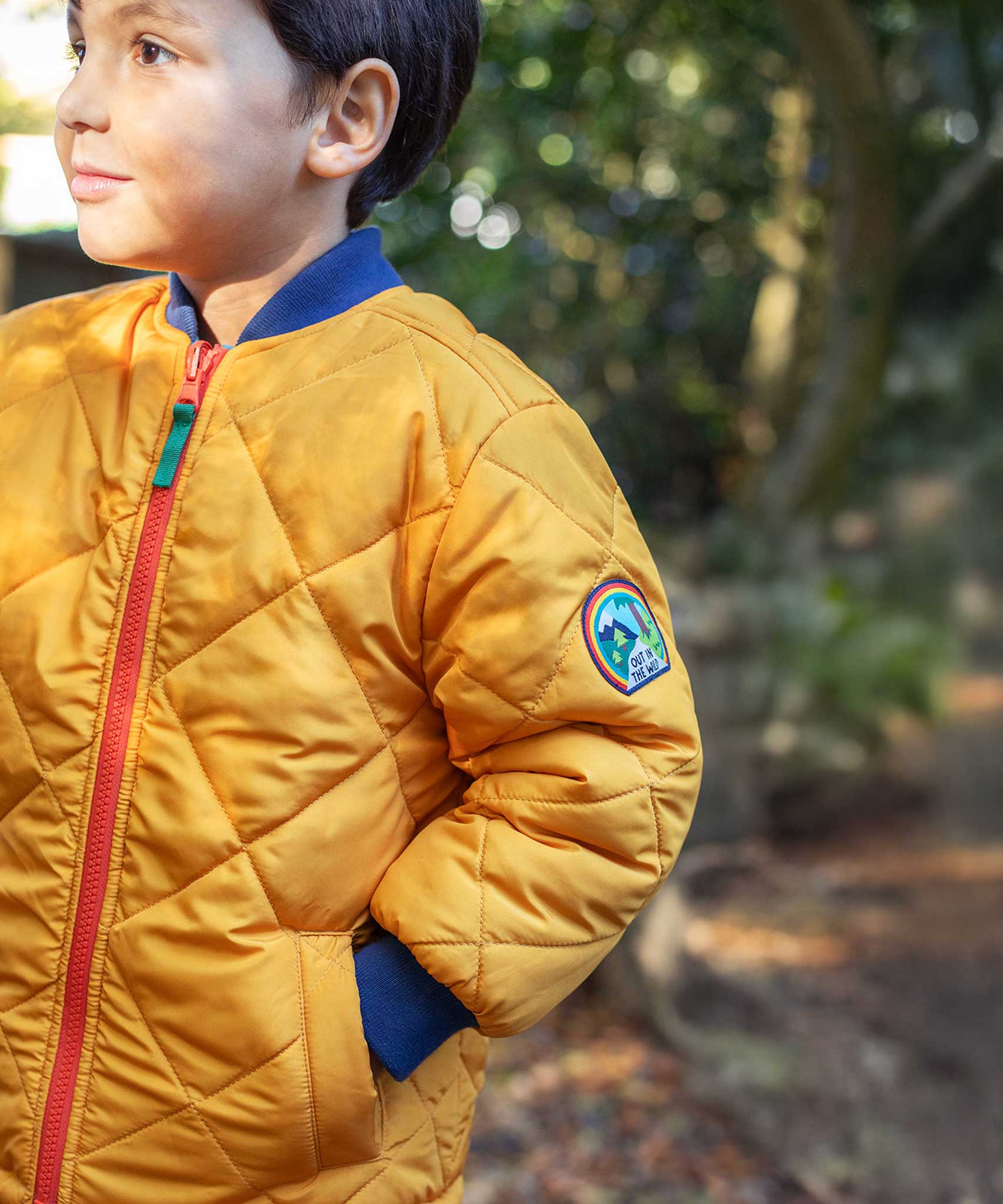 A child wearing the Frugi robin reversible quilted jacket in yellow gold with boat blue fleece.