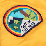 A close up of the 'out in the wild' badge that is on the arms of the Frugi robin reversible quilted jacket in yellow gold with boat blue fleece.