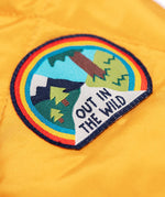 A close up of the 'out in the wild' badge that is on the arms of the Frugi robin reversible quilted jacket in yellow gold with boat blue fleece.