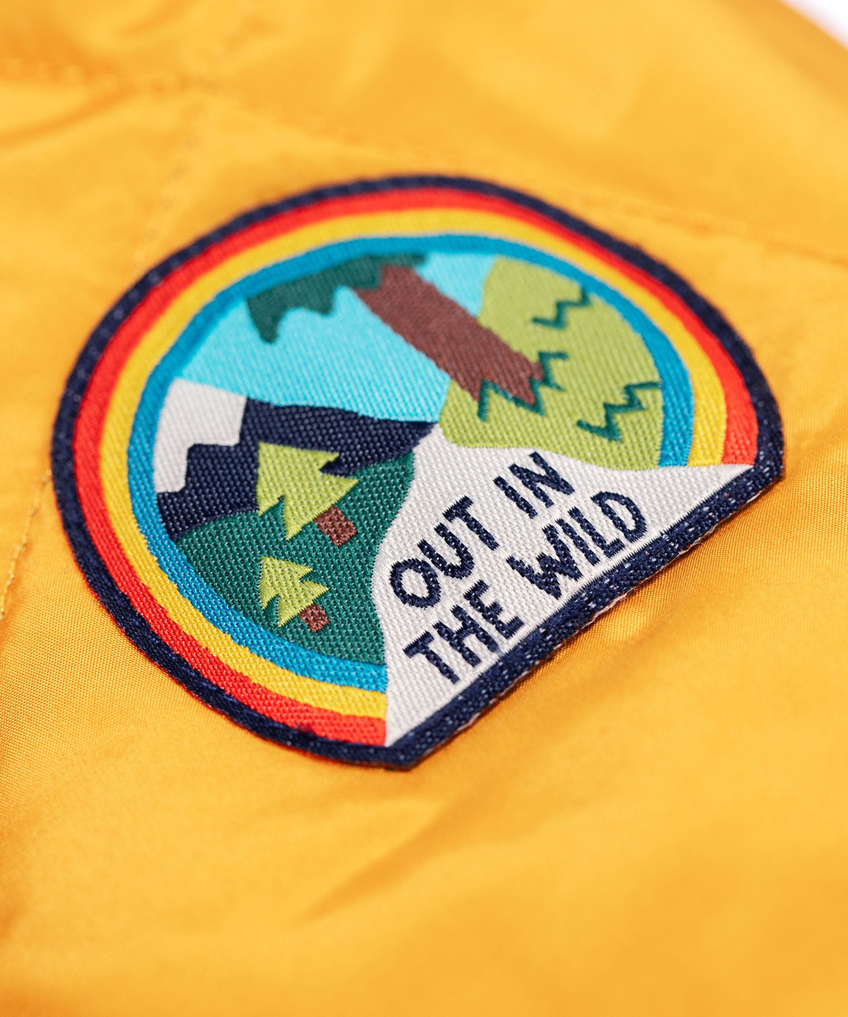 A close up of the 'out in the wild' badge that is on the arms of the Frugi robin reversible quilted jacket in yellow gold with boat blue fleece.