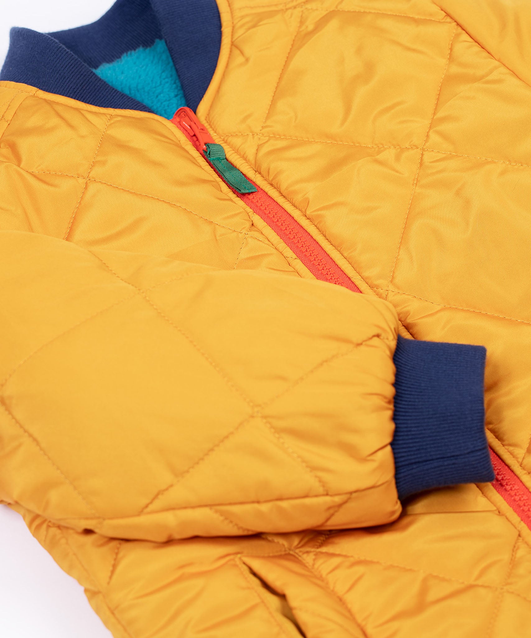 A close up of the navy cuffed sleeves on the Frugi robin reversible quilted jacket in yellow gold with boat blue fleece.