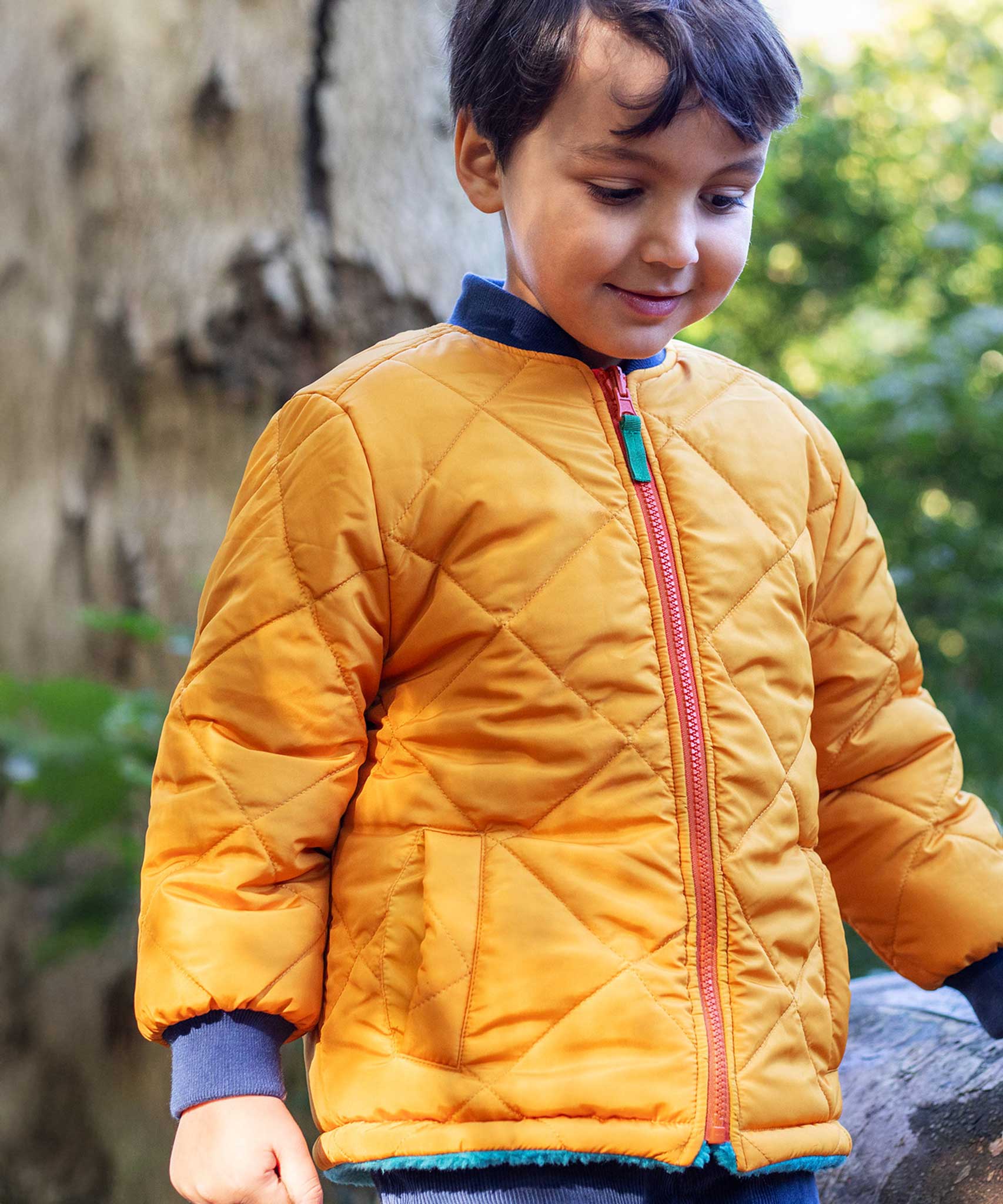 A child wearing the Frugi robin reversible quilted jacket in yellow gold with boat blue fleece.