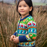 Child wearing the Frugi Robyn fairisle cardigan with colourful farm design featuring tractors, highland coos and puffins. Button up front and navy cuffs, neck and waist band. 