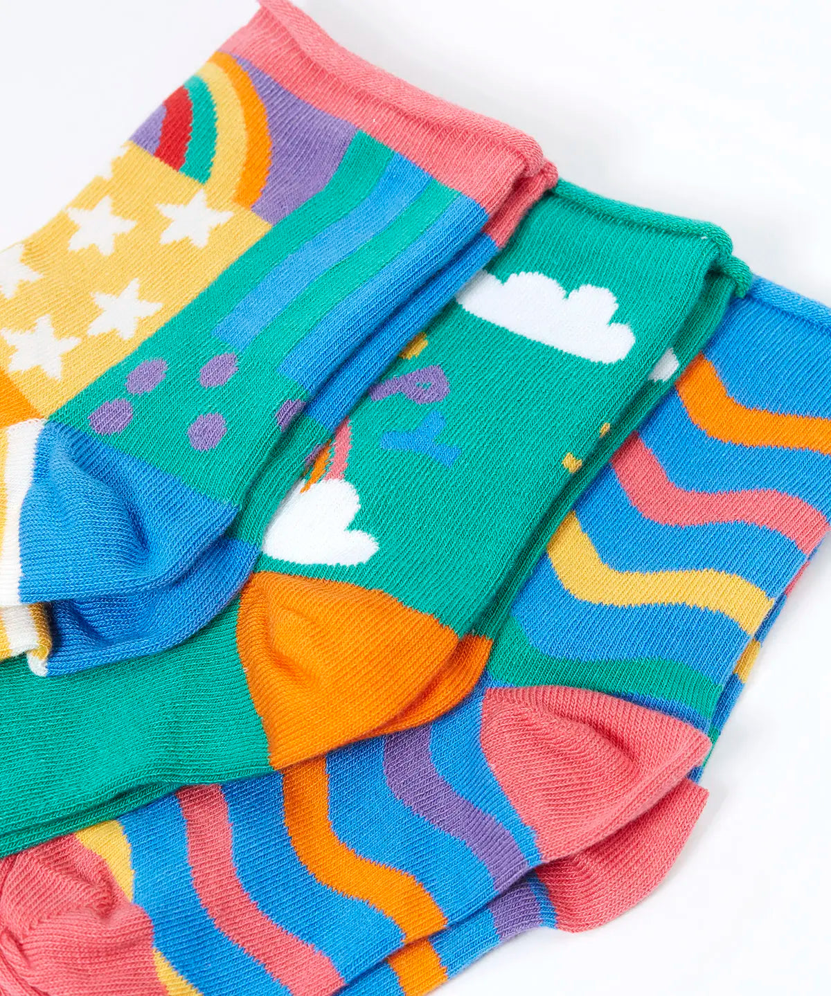 Close up of the Frugi little roly bamboo socks in a 3 pack with rainbow designs. Rainbow wave stripe pair, green with happy rainbow pair and a patchwork pattern pair.