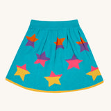 The Frugi Rory Reversible organic cotton kids Skirt with a Rainbow Stars design shown on the turquoise blue side with multicolored stars. 