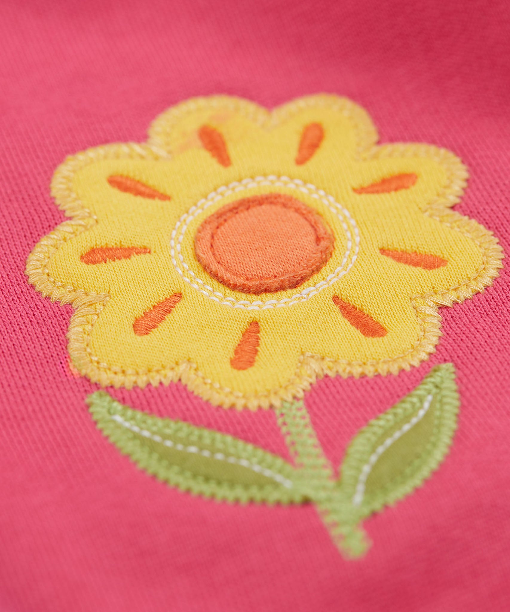 A close up of the yellow flower applique on the knee of the Frugi rose pink coloured flower and mushroom crawlers kids joggers.