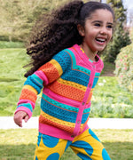 A child running in a park and wearing the Frugi kids rowe rainbow cardigan in rainbow/pointelle.