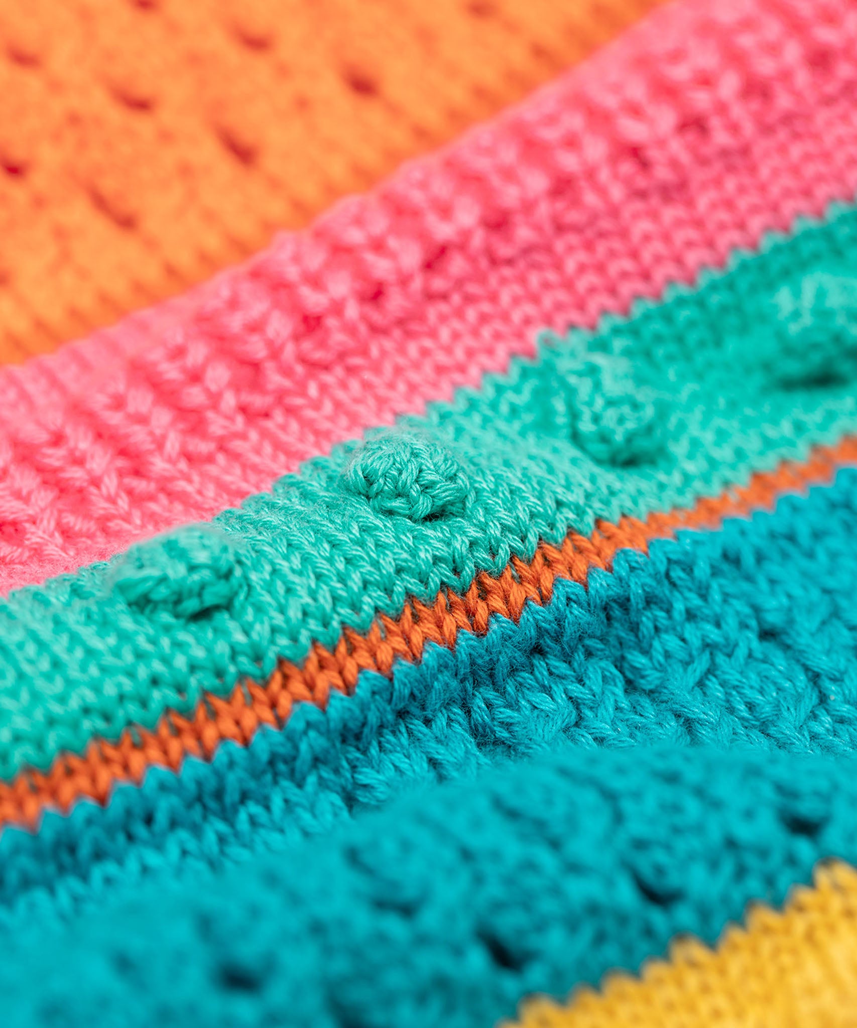 A close up of the Frugi kids rowe rainbow cardigan in rainbow/pointelle showing the soft knit pom pom pattern detail