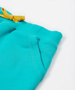 Close up of the Frugi kids sea moss Samson shorts showing the yellow waist drawstring and front pocket detail on turquoise organic cotton fabric