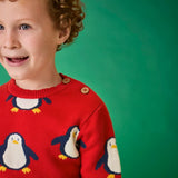 Child wearing the Frugi scarlet penguins organic cotton jolly knitted jumper. Red knitted jumper with repeat penguin print and rainbow stripe hemline and arm cuffs. Close up of the button closure on the shoulder. 