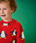 Child wearing the Frugi scarlet penguins organic cotton jolly knitted jumper. Red knitted jumper with repeat penguin print and rainbow stripe hemline and arm cuffs. Close up of the button closure on the shoulder. 