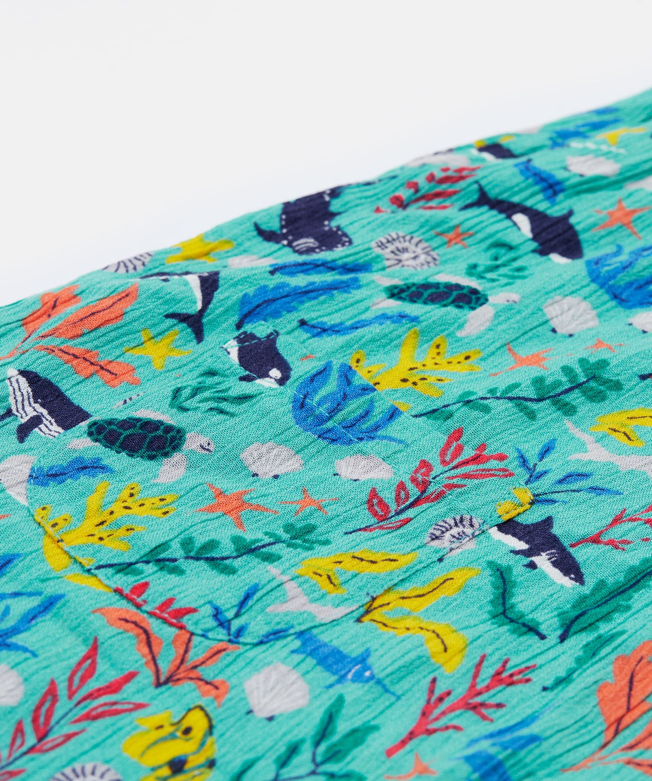 A close up of the Frugi Maris Playsuit, with a Sea Life print which includes different sea animals and colourful seaweed and coral, featuring a small pocket.