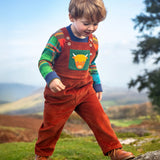 Child wearing the Frugi sebby brown rust organic cotton cord dungaree with a green chest pocket featuring a highland cow applique with a knitted jumper underneath.