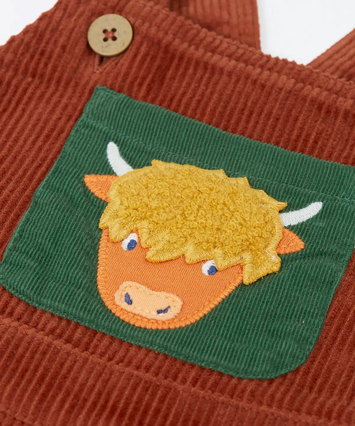 Frugi brown rust organic cotton cord dungaree laid flat showing close up of a green chest pocket with highland cow applique on the front