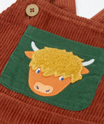 Frugi brown rust organic cotton cord dungaree laid flat showing close up of a green chest pocket with highland cow applique on the front