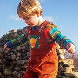 Child wearing the Frugi sebby brown rust organic cotton cord dungaree with a green chest pocket featuring a highland cow applique with a knitted jumper underneath.