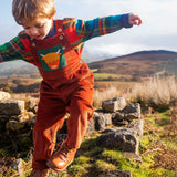 Child wearing the Frugi sebby brown rust organic cotton cord dungaree with a green chest pocket featuring a highland cow applique with a knitted jumper underneath.