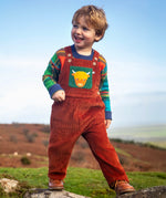 Child wearing the Frugi sebby brown rust organic cotton cord dungaree with a green chest pocket featuring a highland cow applique with a knitted jumper underneath.