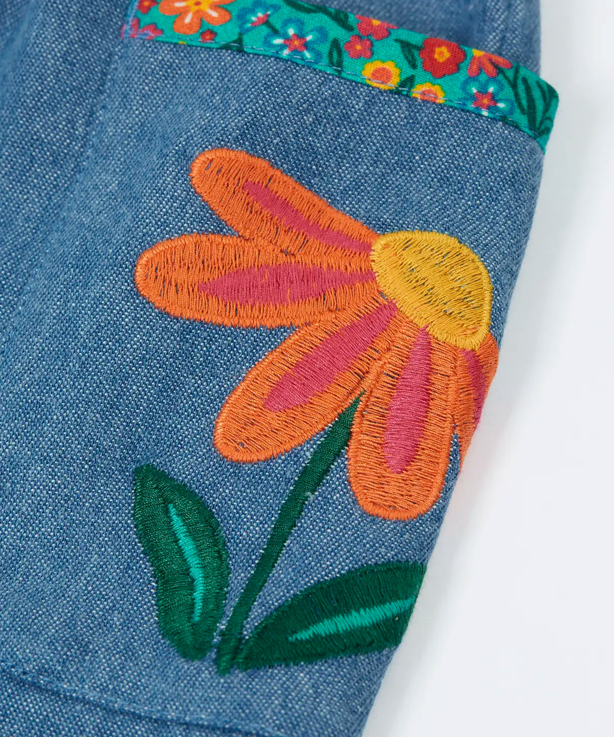 Close up of an embroidered flower on the side pockets of the Frugi Selena child's denim skirt with wildflower trims.