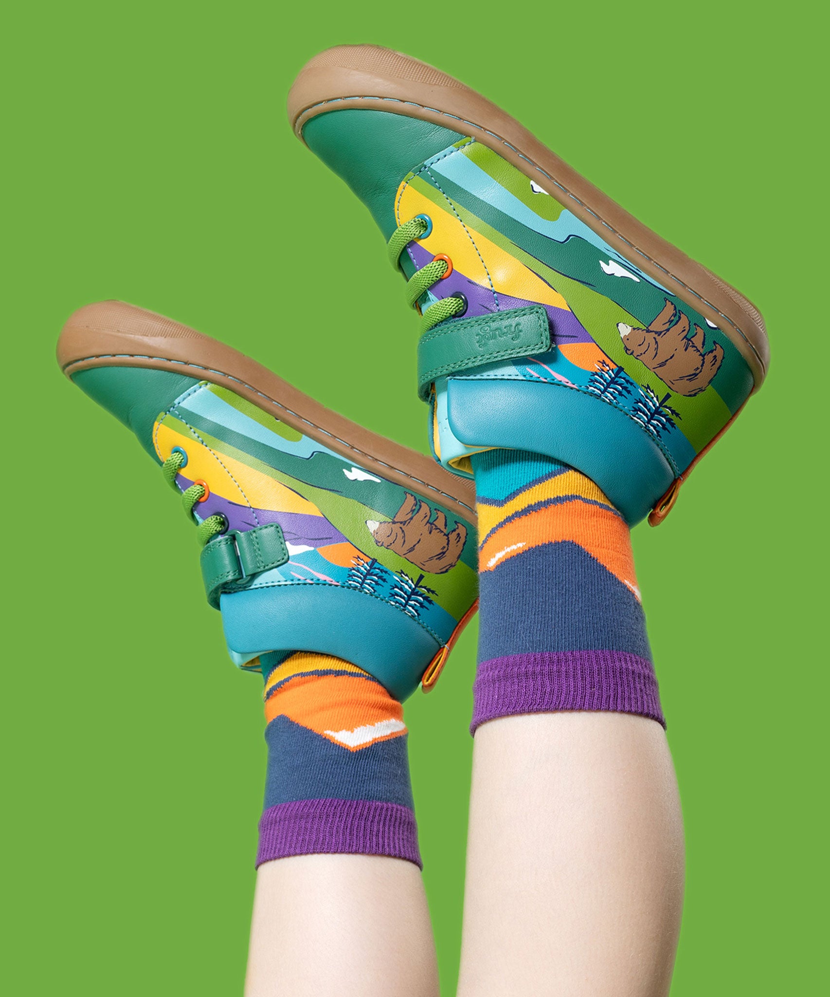 A child wearing the Frugi Sky Stretch children's leather Lace Boot with a holly green bear design with Frugi organic cotton socks featuring a mountian outline design. Check out our range of kids shoes and socks here at Babipur.