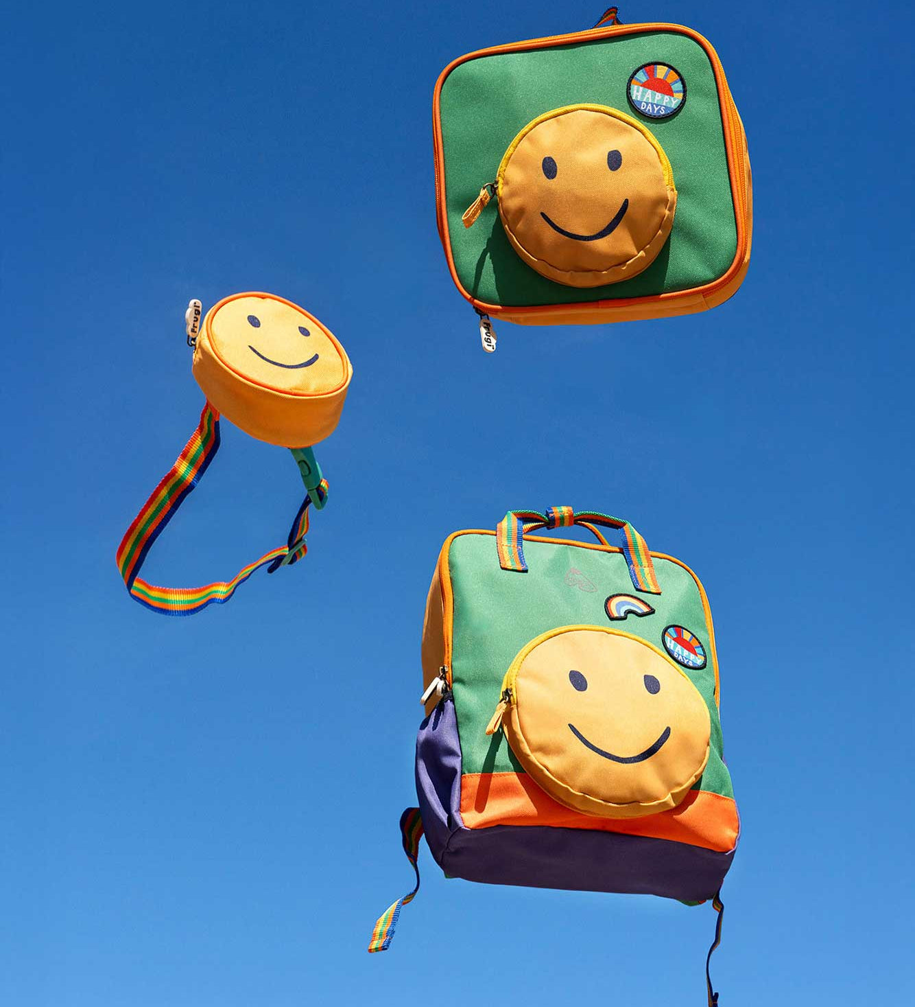 Frugi happy smiley face children's belt bag, lunch bag and backpack shown on a sky blue background. Circular shaped yellow pockets decorated with a smiley face with rainbow coloured straps.
