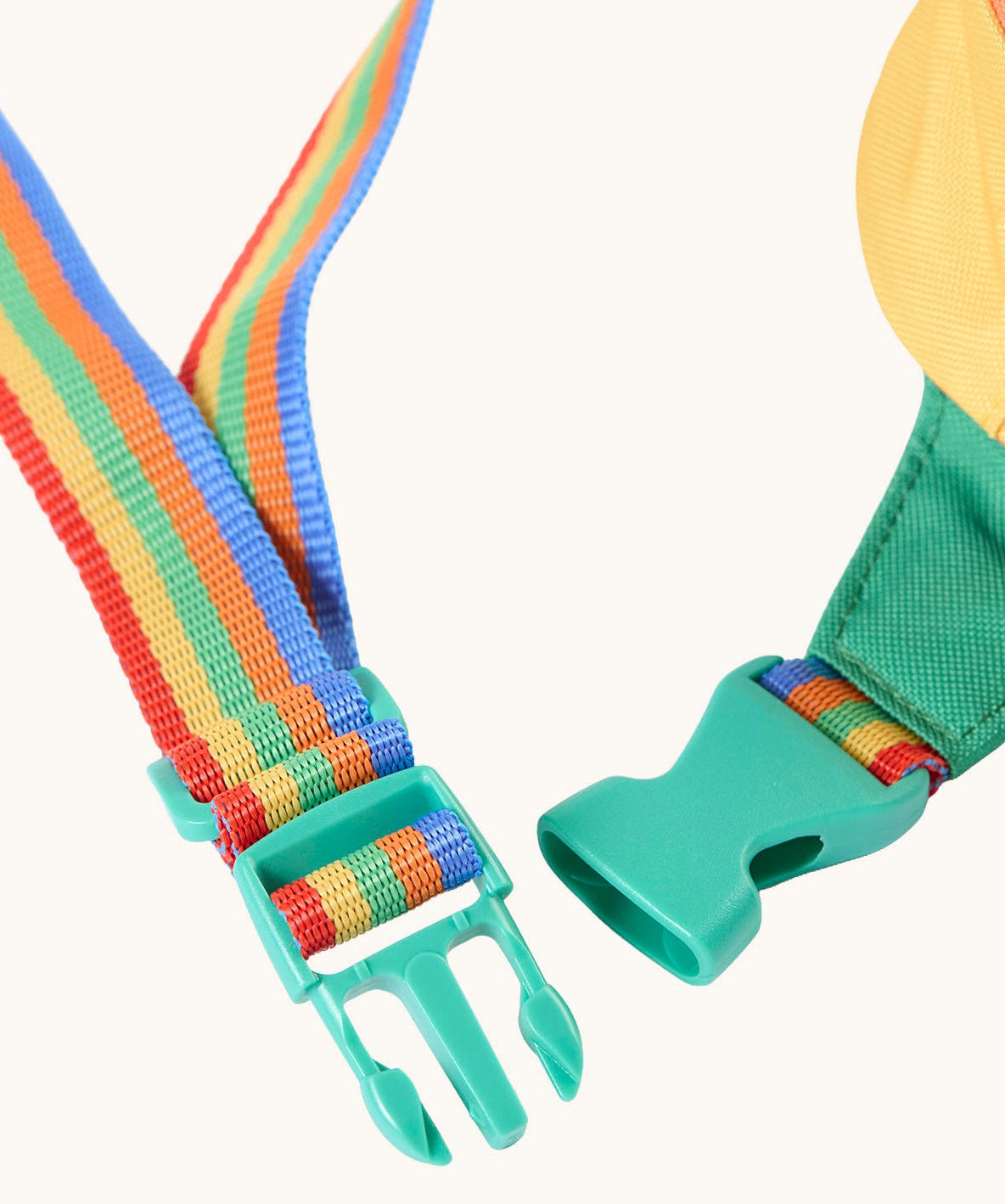 A close up of the green coloured quick release buckle closure on the rainbow coloured strap of the Frugi smiley face children's belt bag. 