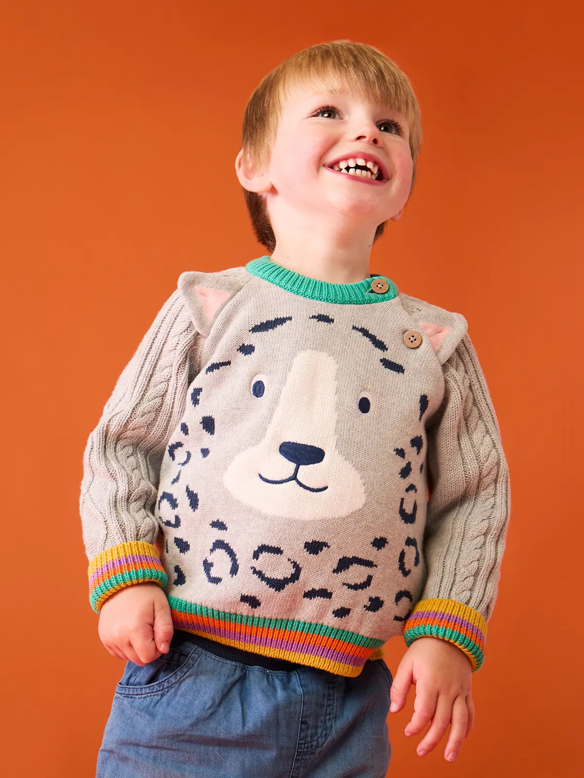 Child wearing the Frugi snow leopard organic cotton character knit jumper with 3d ears, green neck trim and rainbow arm cuffs and hemline. 