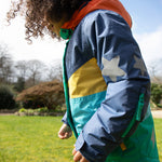 A child smiling and wearing the Frugi Snow & Ski Coat - Iguana Colourblock