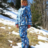 A child wearing the Frugi Snow and Ski Salopettes in a Penguin Waddle design on a blue background with matching ski jacket. 
