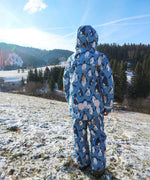 A child facing away from teh camera wearing the Frugi Snow and Ski Salopettes in a Penguin Waddle design with matching ski coat with the hood up.