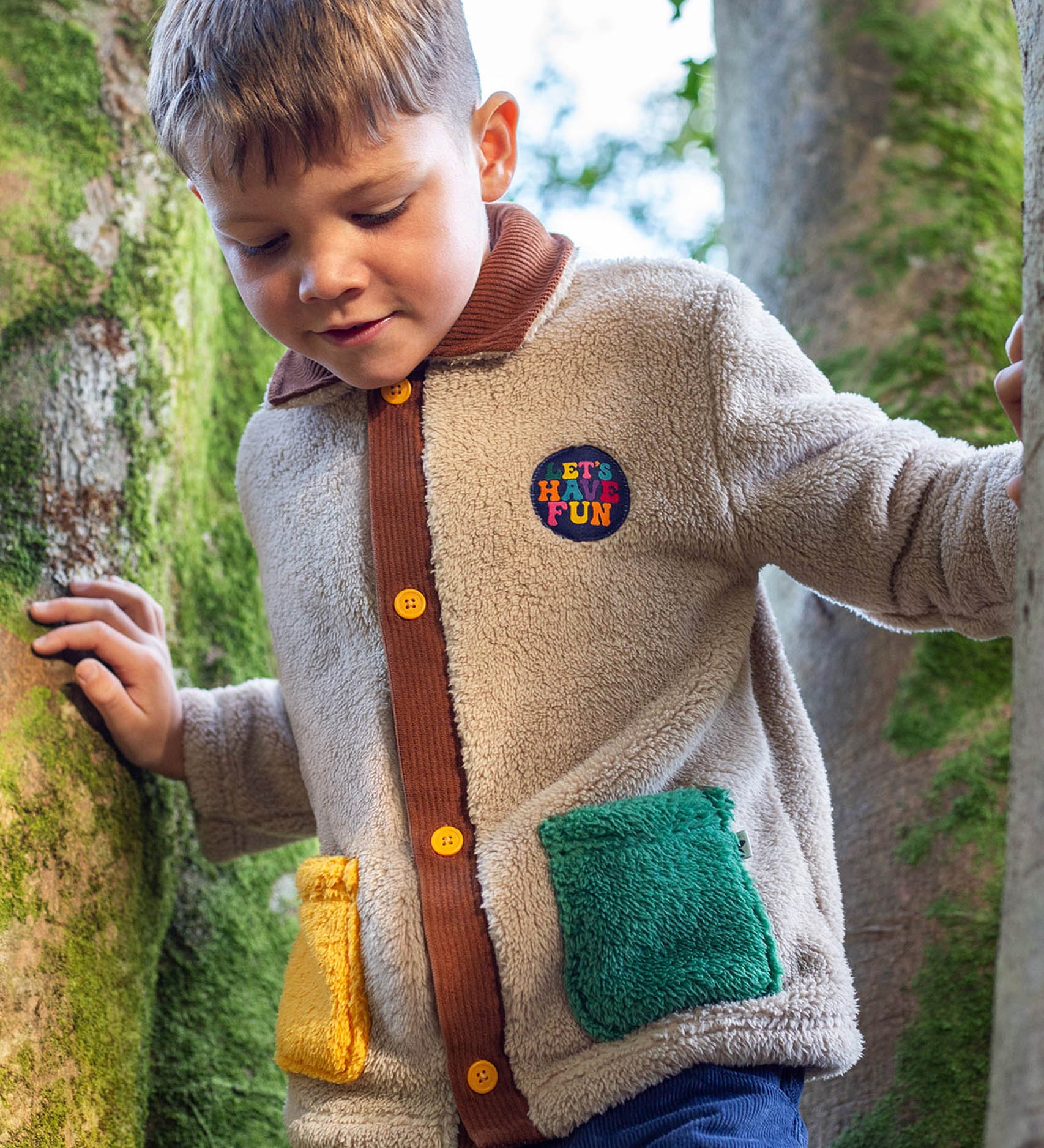 A child walking through by trees and wearing the Frugi kids snuggly cord jacket in twig/hotchpotch.